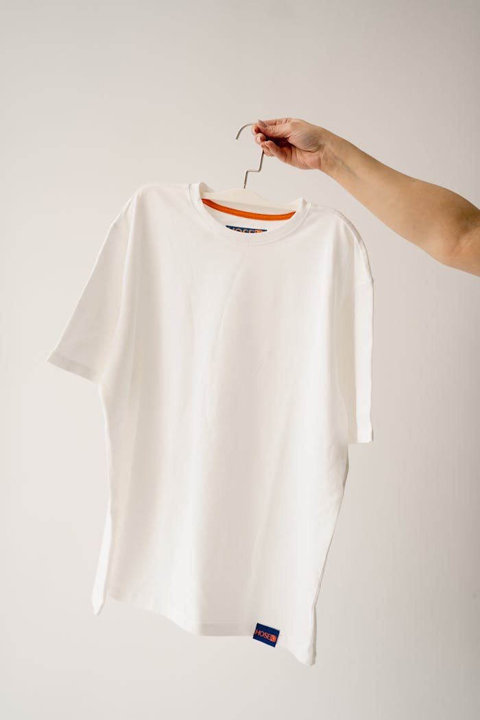 Clean white t-shirt on hanger held by human hand against a white studio background.